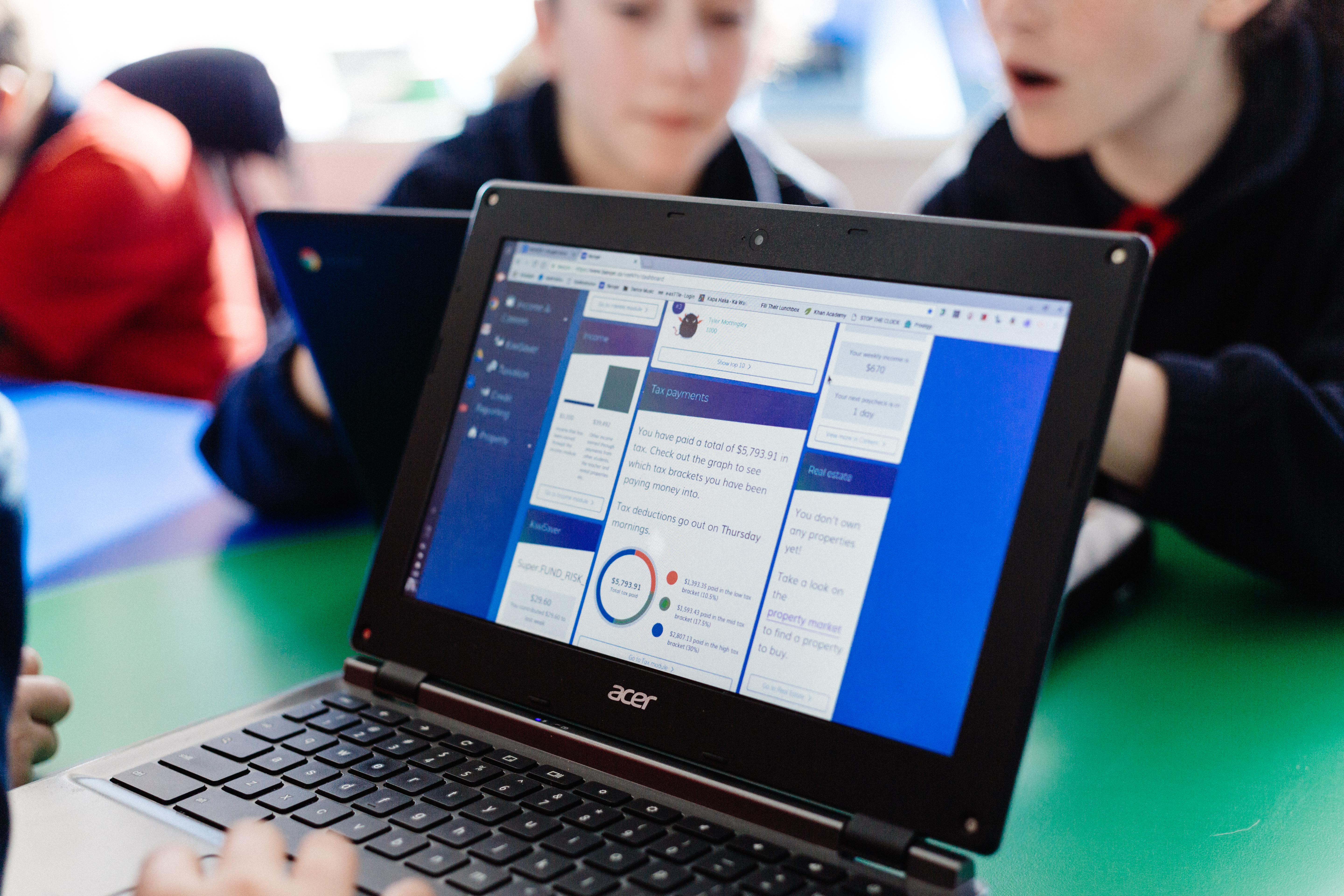 image of a computer displaying banqer primary with students in the background