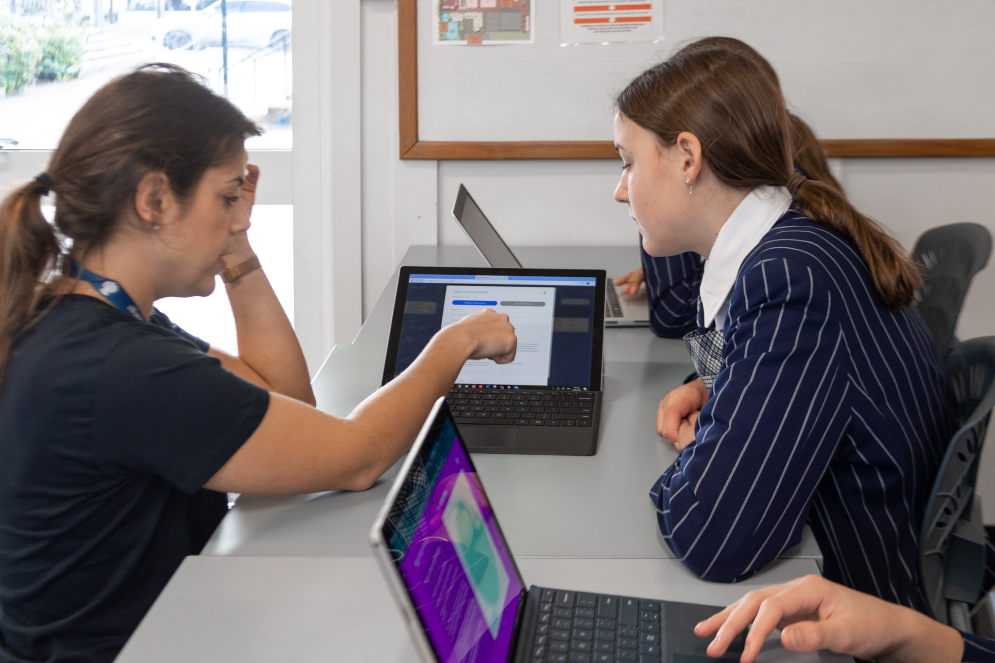 female student and female teacher in a classroom using banqer on a laptop