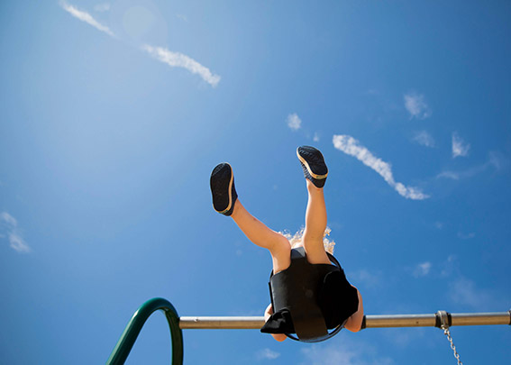 View from below of a child on a playground swing, against a bright blue sky.